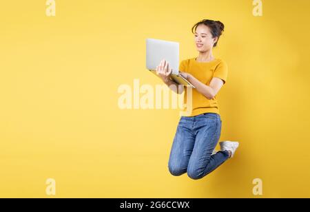 Full body profile photo of young asian girl jumping high holding a laptop writing a new social media post, isolated on blue background Stock Photo
