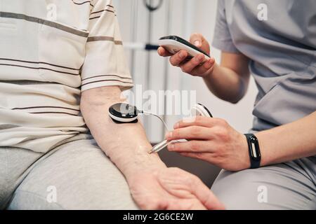 Male physiotherapist measuring muscle activity with testing unit Stock Photo