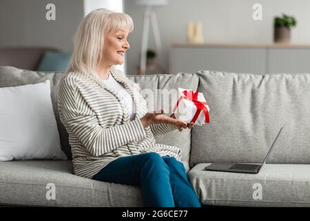 Smiling Mature Woman Holding Present Box Making Video Call Stock Photo