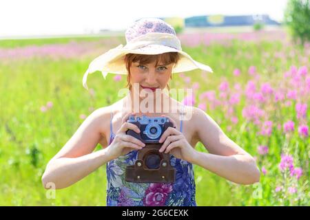 Portrait of a young woman with a camera in a hat in a field of red flowers on a hot summer day. Selective focus. Close-up Stock Photo