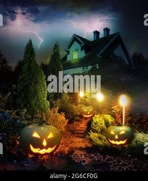 Thunderstorm on Halloween evening, pumpkin lanterns pathway throug mystery garden to scary haunted house Stock Photo