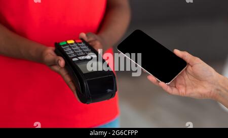 Black delivery man in uniform holding POS machine for payment Stock Photo