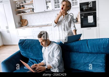 Serious tired millennial spouses engaged manage family finances budget. Tired exhausted couple sit on sofa at home office working on laptops online Stock Photo
