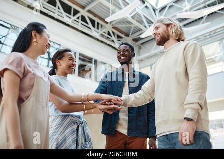 Side view at diverse group of happy young people stacking hands outdoors and celebrating friendship, copy space Stock Photo