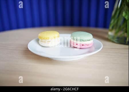 Two delicious macarons on a wooden surface against the background of an embossed blue wall. Sweet food theme. Still life Stock Photo
