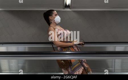 Perspective effect of a young woman with a face mask in a leaning position going down an escalator. Funny perspective Stock Photo