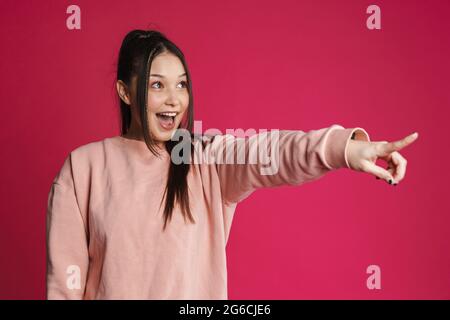 Asian excited woman smiling and pointing finger aside isolated over purple wall Stock Photo