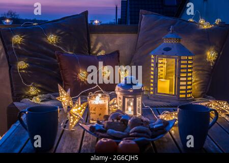 Cozy sitting area with coffee and cookies on a balcony, decorated for winter with lanterns, candles, woolen blankets and fairy lights Stock Photo