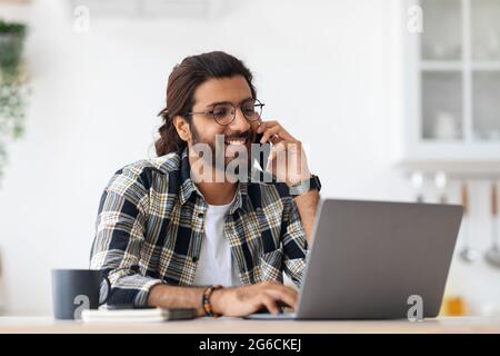 Smiling arab man freelancer talking on phone and taking notes Stock Photo