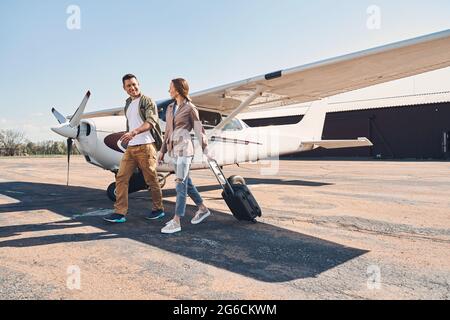 Cheerful couple with travel bags walking down airfield Stock Photo