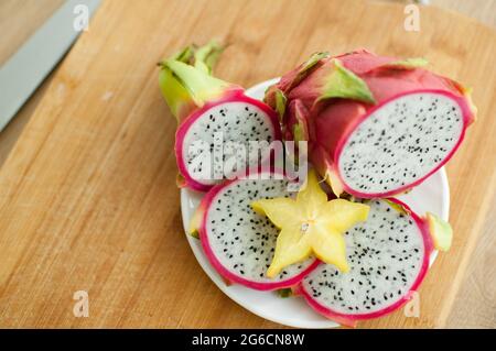 Slices of dragon fruit or pitaya with white pulp and black seeds on white plate with one slice of starfruit or averrhoa carambola. Exotic fruits Stock Photo
