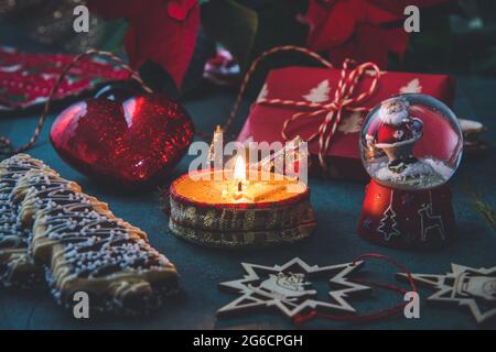 Christmas candle with gingerbread cookies, decorations and poinsettia plant on a dark green background Stock Photo
