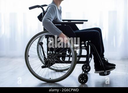Disability in teenagers concept. Side view of unrecognizable impaired teen boy sitting in wheelchair at home, closeup Stock Photo
