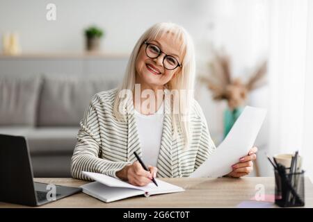 Smiling mature woman writing and holding document at home Stock Photo