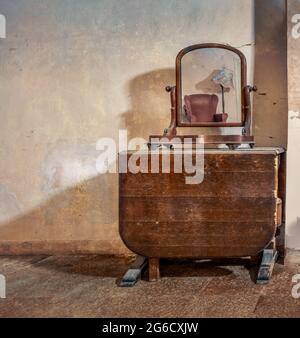 Mirror on old table reflecting chair, lamp. Vintage, retro furniture items in abandoned old derelict house. Stock Photo