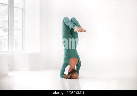 Full body of focused slim female female performing handstand near wall while practicing yoga in light room Stock Photo