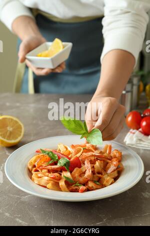 Woman chef putting basil on pasta with shrimps, close up Stock Photo