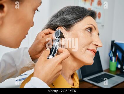 Hearing test for mature people, otoscopy. Otolaryngologist doctor checking senior woman's ear using otoscope or auriscope at medical center Stock Photo