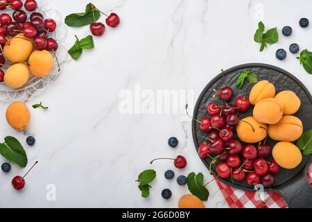 Fresh apricots, red cherry and blackberry on white marble background. Vegetarian, weight loss, clean and healthy eating concept. Top view. Copy space. Stock Photo
