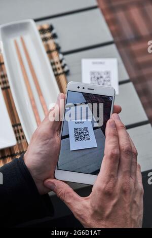 From above of crop unrecognizable male using smartphone and scanning QR code of menu of restaurant Stock Photo