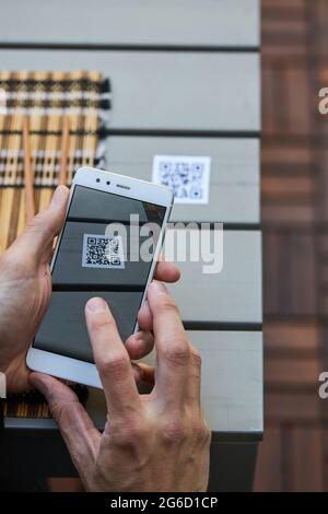 From above of crop unrecognizable male using smartphone and scanning QR code of menu of restaurant Stock Photo