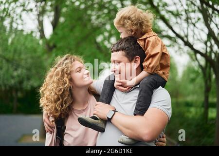 Delighted loving couple with adorable child spending time together in summer park and enjoying weekend Stock Photo