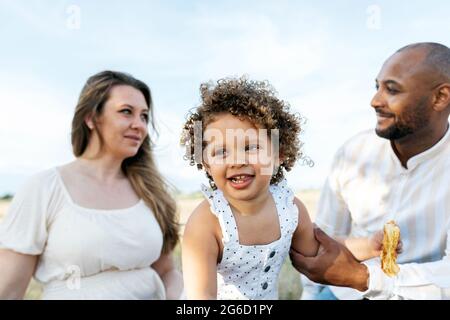 Happy multiethnic family with cute little daughter enjoying summer picnic in nature Stock Photo