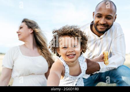 Happy multiethnic family with cute little daughter enjoying summer picnic in nature Stock Photo