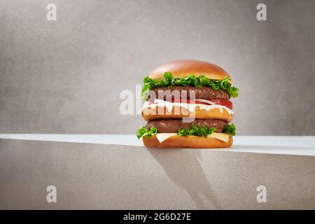 Tasty double burger with cutlets and fresh lettuce and delicious cheese served on gray background Stock Photo
