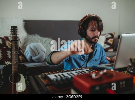 Young man in headphones using synthesizer and laptop at table at home Stock Photo
