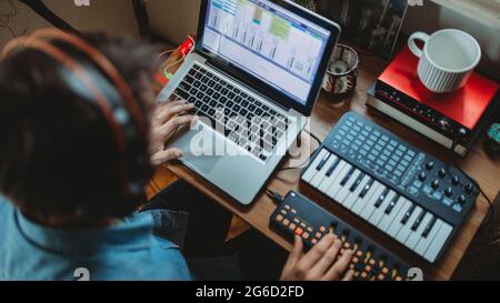 From above unrecognizable of focused young man in headphones working on synthesizer and laptop at table at home Stock Photo