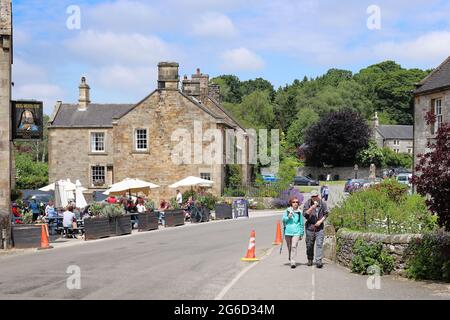 Hartington, Peak District, Derbyshire, England, UK - A couple eating ice cream and tourist crowd sit outside pub on a summer day in the village Stock Photo
