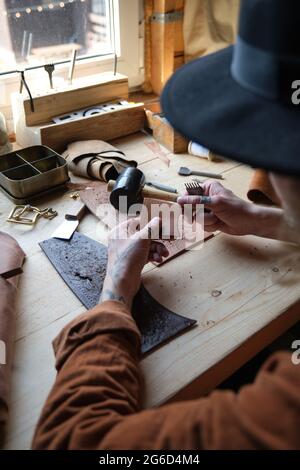 Close-up of carpenter sitting at the table and working with leather, he repairing products Stock Photo