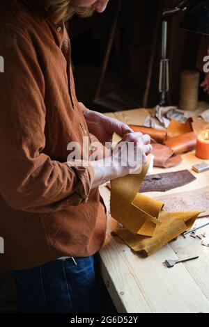 Close-up of craftsman holding pieces of leather textile in his hands and making products in workshop Stock Photo