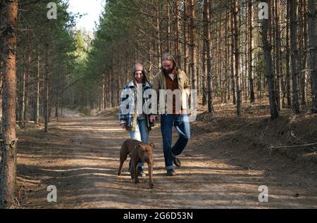 Young couple holding hands and walking together with their dog in the park Stock Photo