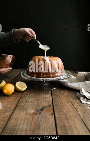 Crop view of hand coating with a spoon a lemon sponge cake placed on a wooden table against a dark background Stock Photo