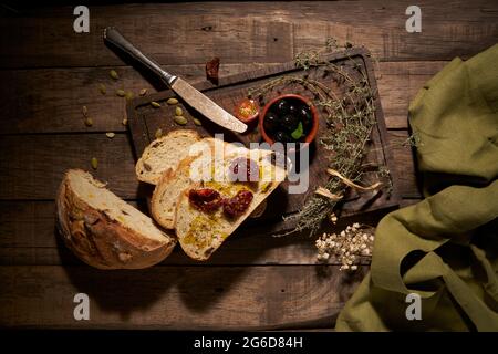 Top view composition of sliced homemade round bread served with aromatic sun dried tomatoes on wooden table with herbs Stock Photo