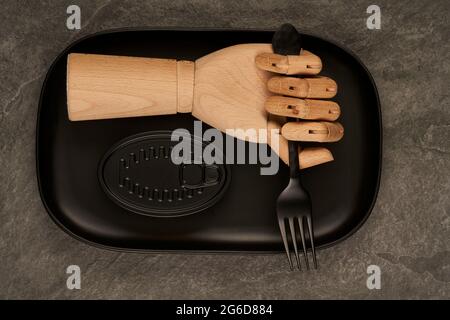 Artificial lumber hand with fork placed on tray near sealed black can with preserves on table Stock Photo