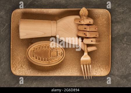 Artificial lumber hand with fork placed on gold tray near sealed can with preserves on table Stock Photo