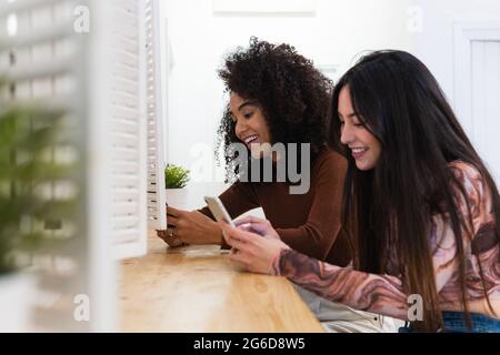 Side view of content diverse female friends sitting at counter in bar and using smartphones while enjoying weekend together Stock Photo