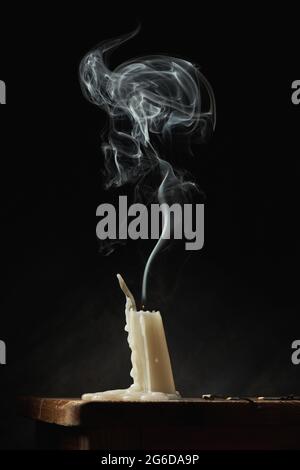 Smoke over white extinguished candle placed on wooden table on black background in studio Stock Photo