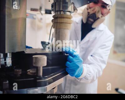 Male worker in protective uniform operating capsule filling machine at pharmaceutical manufacturing plant Stock Photo