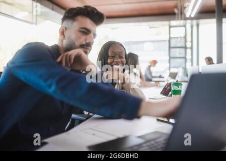 Diverse cheerful coworkers at table with laptop discussing project while working together in contemporary workspace Stock Photo