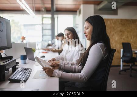 Multiracial female colleagues analyzing diagrams at table while working in modern workspace Stock Photo