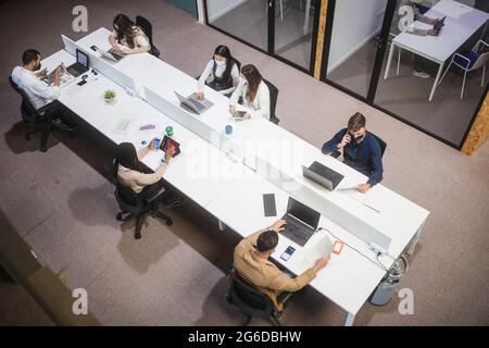 From above of company of people sitting at table and using laptops while working in coworking space Stock Photo