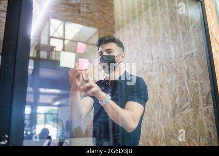 Male executive manager writing on sticky note on glass wall during brainstorm with coworkers in office Stock Photo