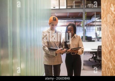 Happy smiling multiethnic female colleagues with tablets standing in coworking space and discussing project Stock Photo