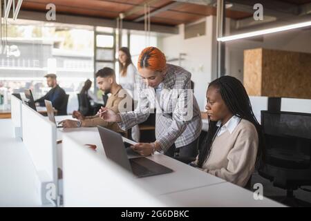 Multiethnic female coworkers discussing project at table while reading documents in modern workplace Stock Photo