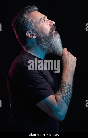 Side view of handsome mature male with gray beard on black background in studio Stock Photo