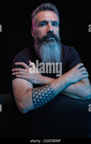 Handsome mature male with gray beard on black background in studio looking at camera Stock Photo